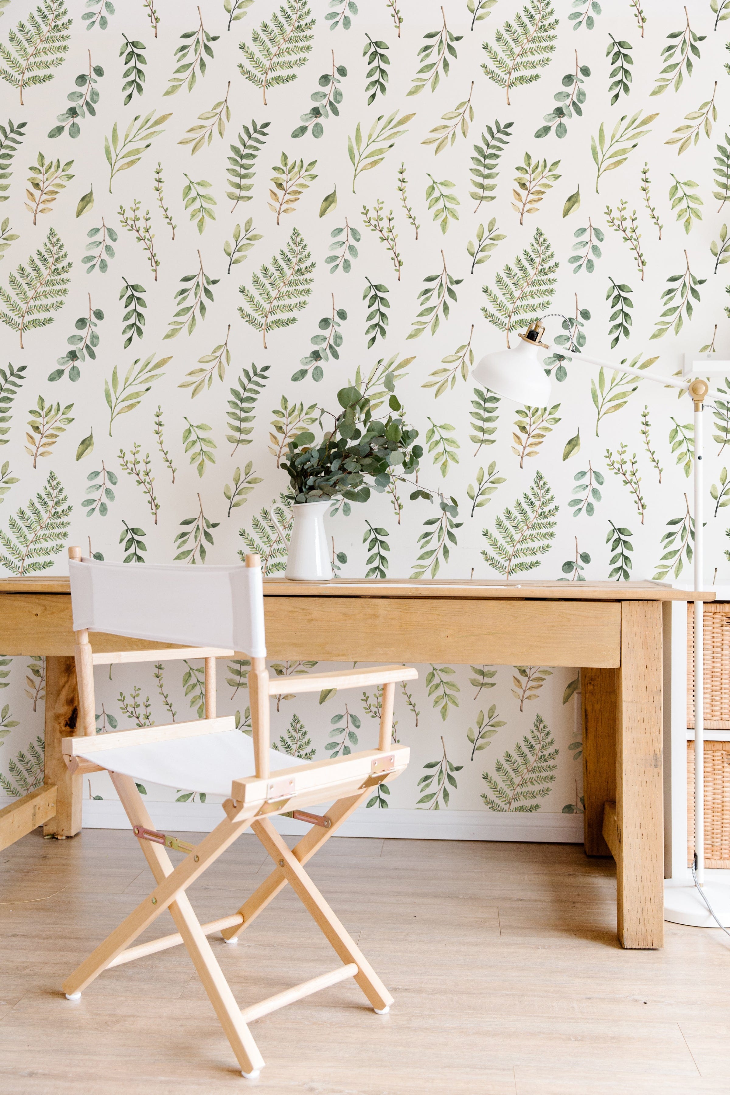 A stylish home office setup featuring Green Foliage Wallpaper with hand-drawn green leaves and branches on a white background, complemented by a wooden desk, a white chair, and a vase of greenery.