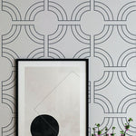 A stylish interior showcases the Geometric Wallpaper, which features bold linear circles interconnected with straight lines in a grayscale color scheme. The abstract geometric pattern adds a modern and sophisticated touch to the decor, highlighted by a framed abstract artwork placed against the patterned wall.