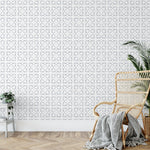 A contemporary room featuring a wall covered in Geometric Watercolour Tile Wallpaper VII, showcasing a sophisticated gray and white repeating tile pattern that adds a modern, artistic touch to the decor, complemented by a natural rattan chair and a potted plant