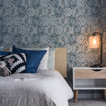 A modern bedroom with a bed dressed in neutral linens, complemented by a Moroccan Tile patterned accent wall in indigo blue, with a bedside table and hanging wall lamp.