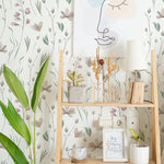 A square image showcasing a creative workspace with Watercolor Floral Wallpaper VII enhancing the background. The decor includes a wooden shelf with artistic and plant elements, harmonizing with the wallpaper's delicate watercolor flowers and contributing to an inspiring and calming environment.