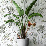 A vibrant indoor plant in a white pot stands against the Green Floral Wallpaper, which features a delicate array of green leaves and fronds, enhancing the fresh and organic atmosphere of the room.