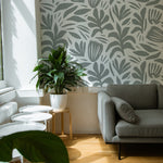 A modern living room enhanced by the Night Train Abstract Floral Wallpaper, adding a touch of elegance with its abstract floral design in gray tones. The room is complemented by a contemporary gray sofa and a vibrant green houseplant.