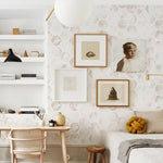 "An interior design setting showcasing a wall adorned with the Watercolour Honeycomb Wallpaper, complemented by a modern minimalist décor including a white bookshelf, a wooden desk with a chair, artwork frames, and cozy textiles."