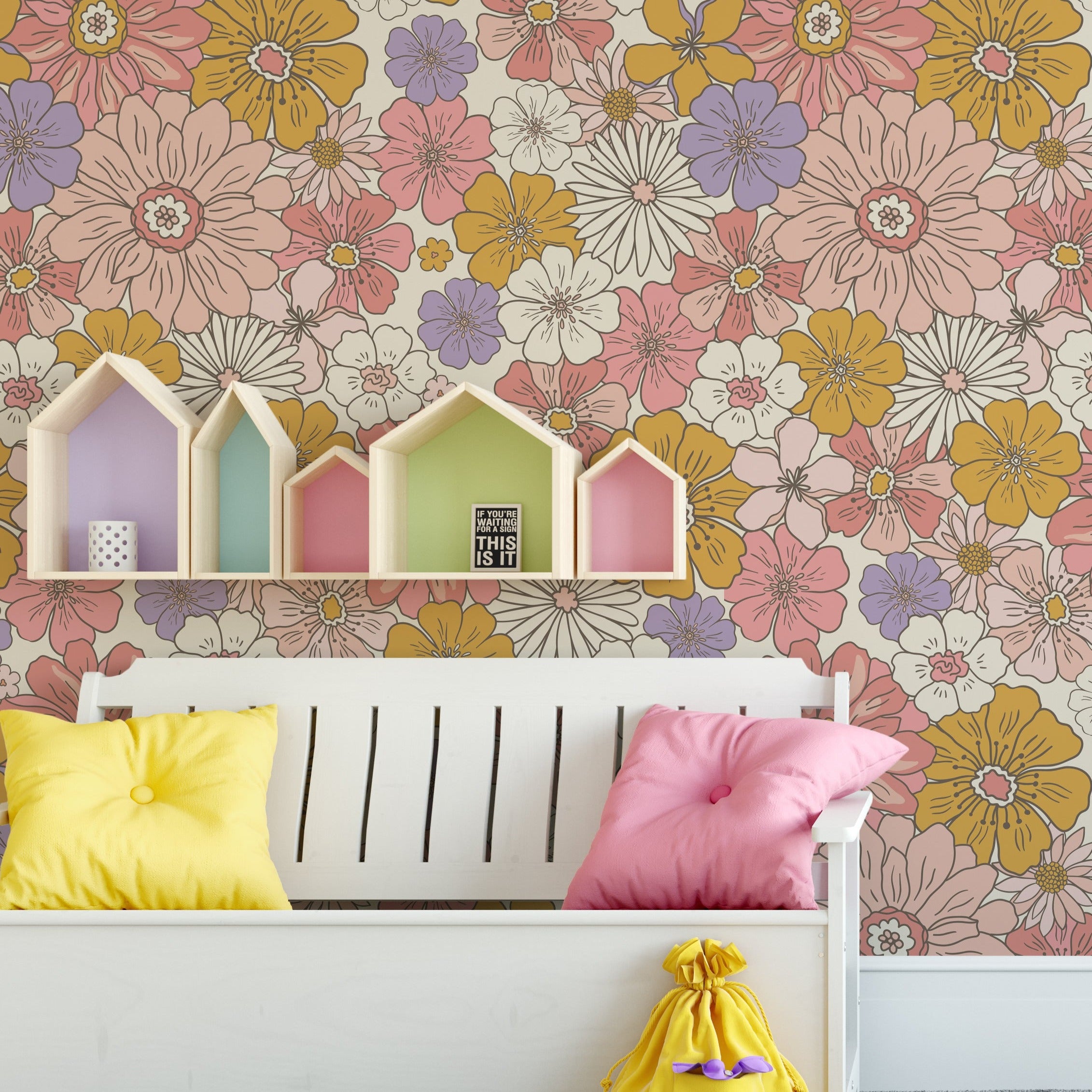 A playful children's room decorated with Retro Groovy Flower Wallpaper, which boasts a colorful floral pattern. The room features a white bed, colorful house-shaped shelves, and a bright interior that complements the lively wallpaper