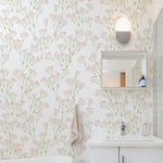 A serene bathroom interior featuring 'Le Marchand de Fleurs Wallpaper', with delicate pink floral stems scattered against a soft white backdrop. The wallpaper provides a fresh and airy feel to the space, complemented by a simple white vanity and a minimalist wall-mounted shelf with decorative items.