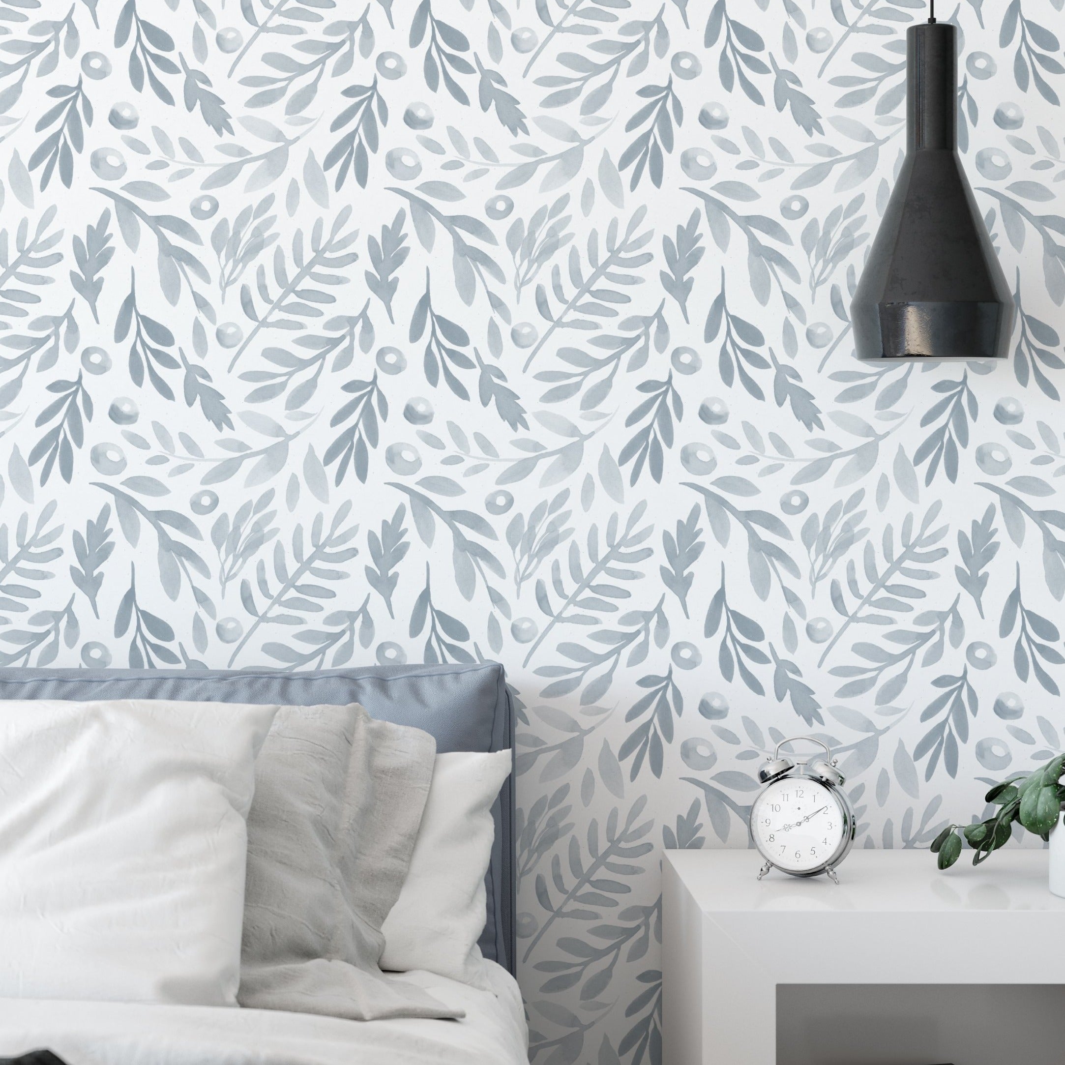 A bedroom setting adorned with 'Watercolor Subtle Botanica - Pale Blue' wallpaper that brings a soothing ambiance to the room. The pale blue leafy design pairs well with the minimalistic bedroom furniture, enhancing the peaceful and restful environment.