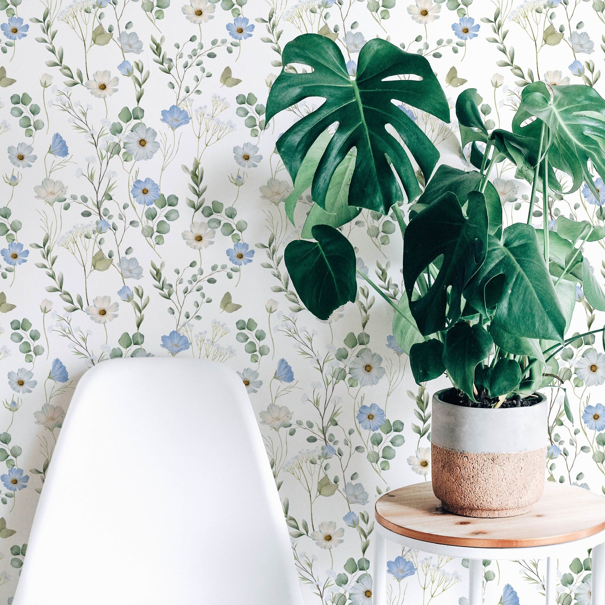 A cozy home office corner is brightened by the Florist Wallpaper, with its lush floral design providing a tranquil backdrop for a white chair and a wooden side table with a potted plant, blending natural elements for a refreshing workspace.