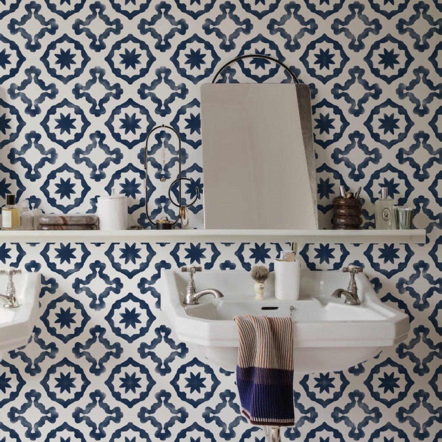 The Geometric Wallpaper XV - Navy elegantly adorns the wall of a well-appointed bathroom. A shelf runs along the wall, hosting a variety of toiletries and bathroom essentials, complementing the striking contrast of the navy blue and white geometric shapes of the wallpaper that command attention.