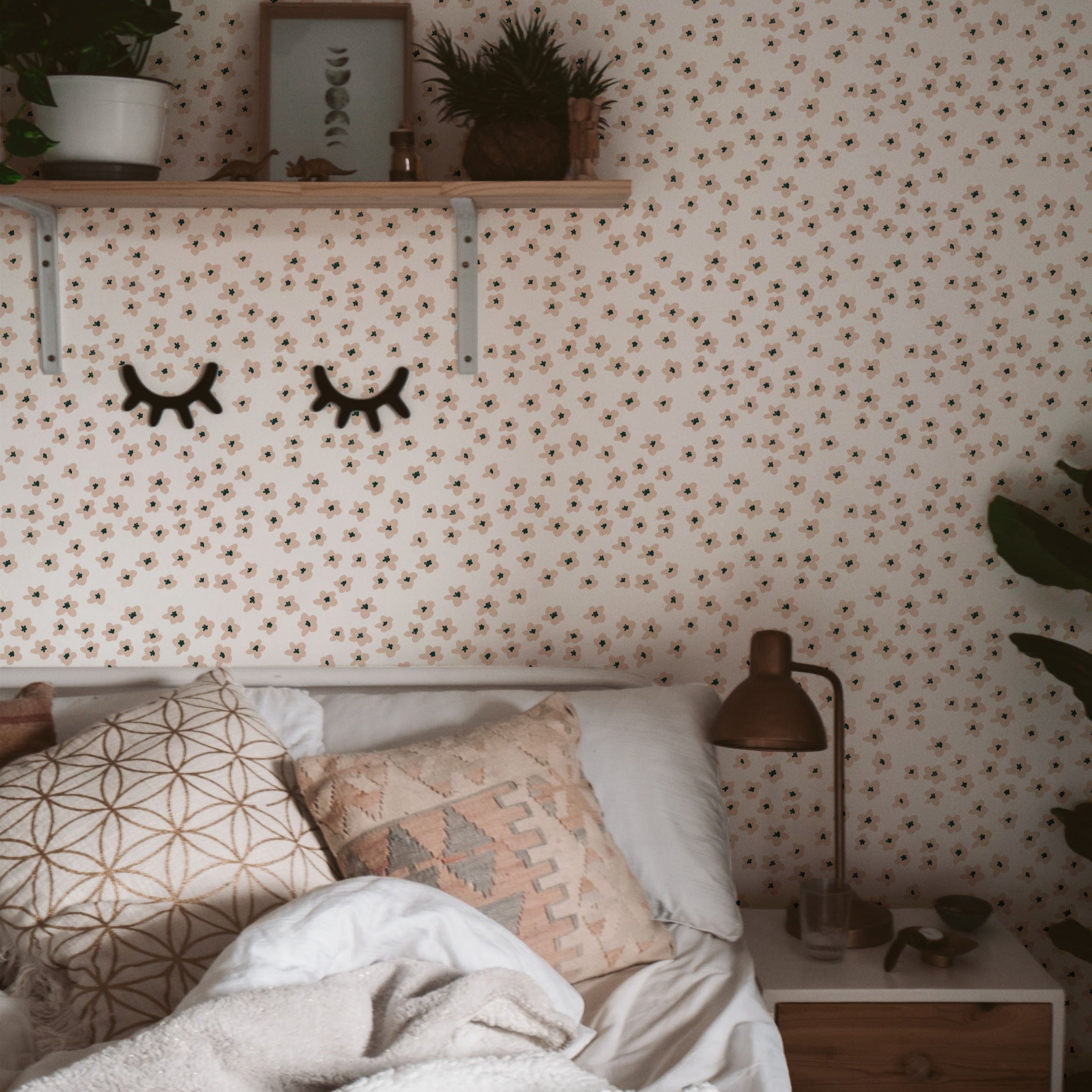 A warmly decorated corner of a bedroom with the Simple Meadow Wallpaper. This setup includes a shelf with decorative items, cozy pillows on the bed, and a small nightstand with a lamp, all complemented by the floral backdrop.