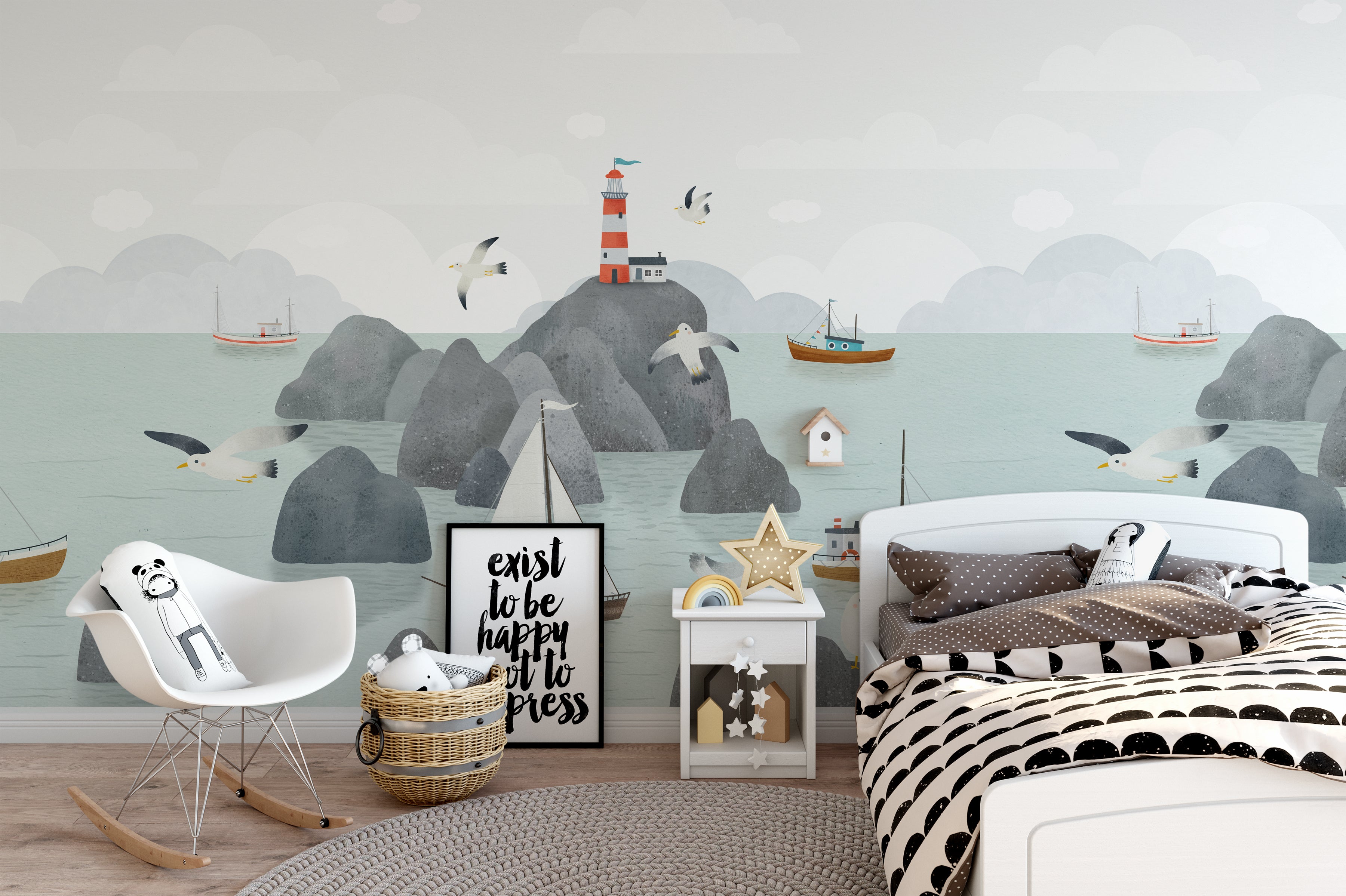 a whimsical children's room with the Kids Nautical Mural Wallpaper creating a charming seaside scene. The wallpaper features soft hues with playful illustrations of sailboats, seagulls, and a lighthouse atop rocky outcrops. The room is styled with a contemporary white bed covered in a black and white striped duvet, a rocking chair with a plush toy, and nautical accents like a star-shaped lamp and decorative sailboat, bringing the joy of a coastal adventure into the space.