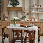 A homely dining area where the Striped Fabric Wallpaper serves as a backdrop, creating a timeless look that complements the natural wood furniture and a white linen-covered table adorned with a vase of fresh tulips