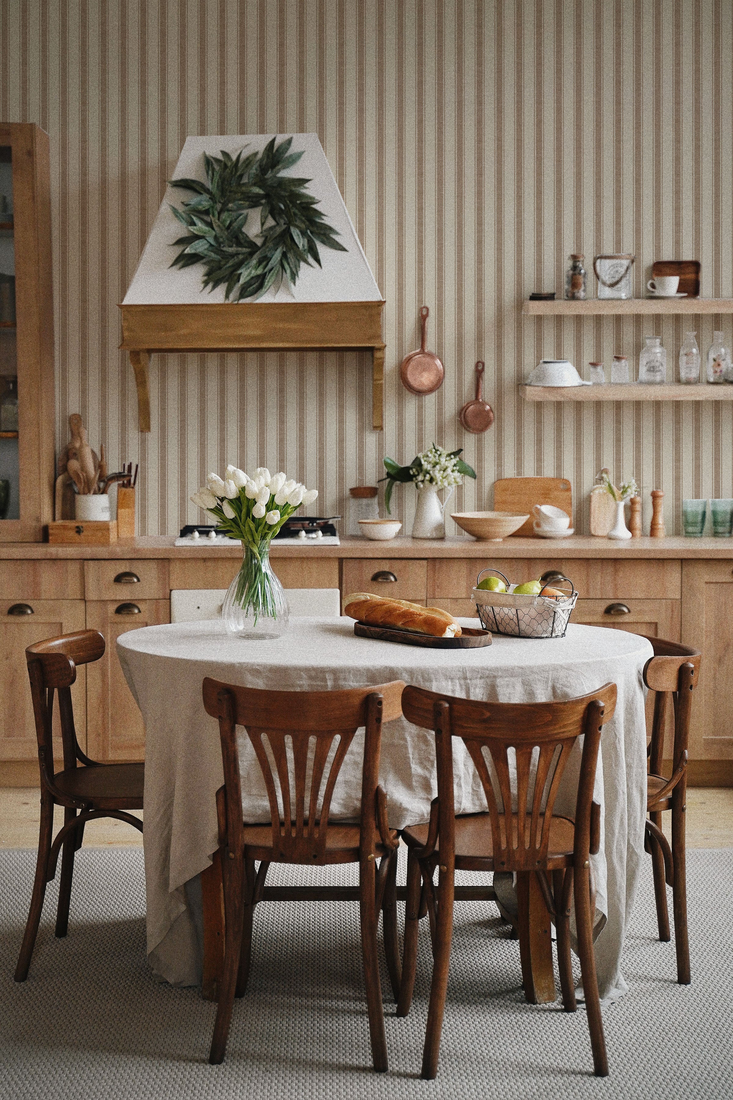 A homely dining area where the Striped Fabric Wallpaper serves as a backdrop, creating a timeless look that complements the natural wood furniture and a white linen-covered table adorned with a vase of fresh tulips
