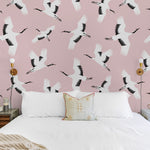 A stylish bedroom showcasing the 'Kids Crane Wallpaper,' with its delicate depiction of white cranes flying over a blush pink background, complementing a modern and serene decor style