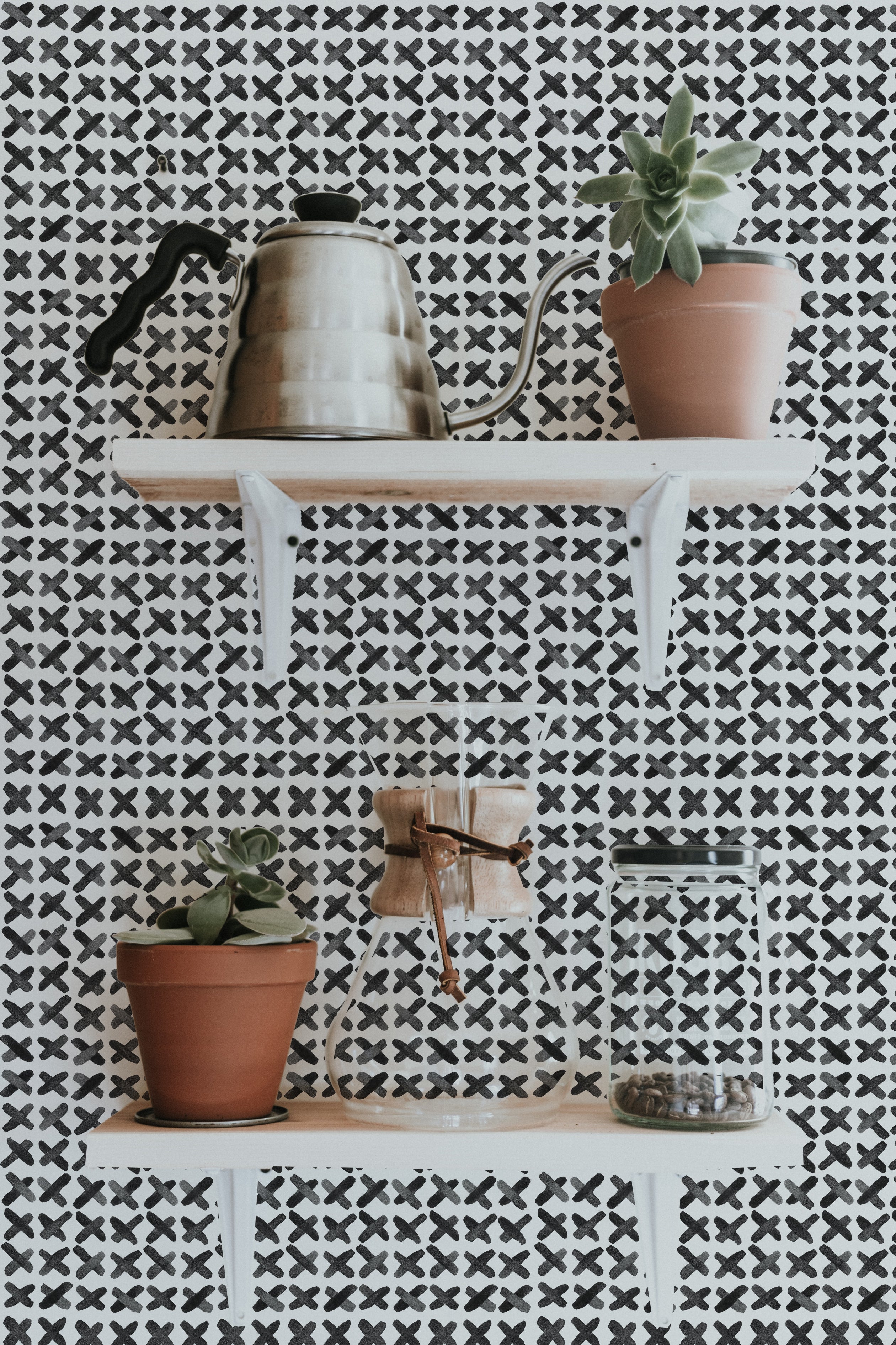Decorative shelf against X Infinity Boho Wallpaper with black and white geometric pattern, displaying a vintage kettle and a potted succulent for a stylish home accent.