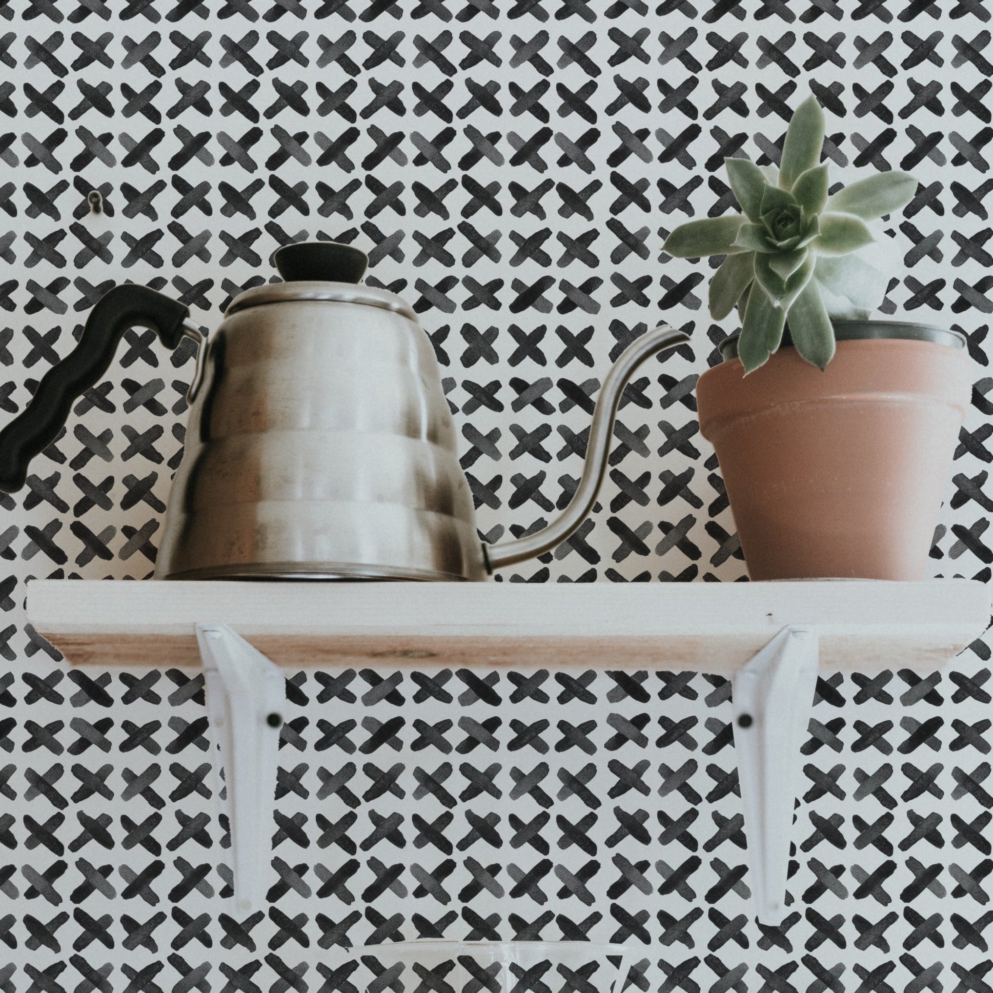 Decorative shelf against X Infinity Boho Wallpaper with black and white geometric pattern, displaying a vintage kettle and a potted succulent for a stylish home accent.