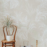 cozy corner of a room featuring the Tropical Palms Wallpaper, with a bentwood chair and a decorative plant, highlighting the cream and beige palm leaf patterns against a light background.