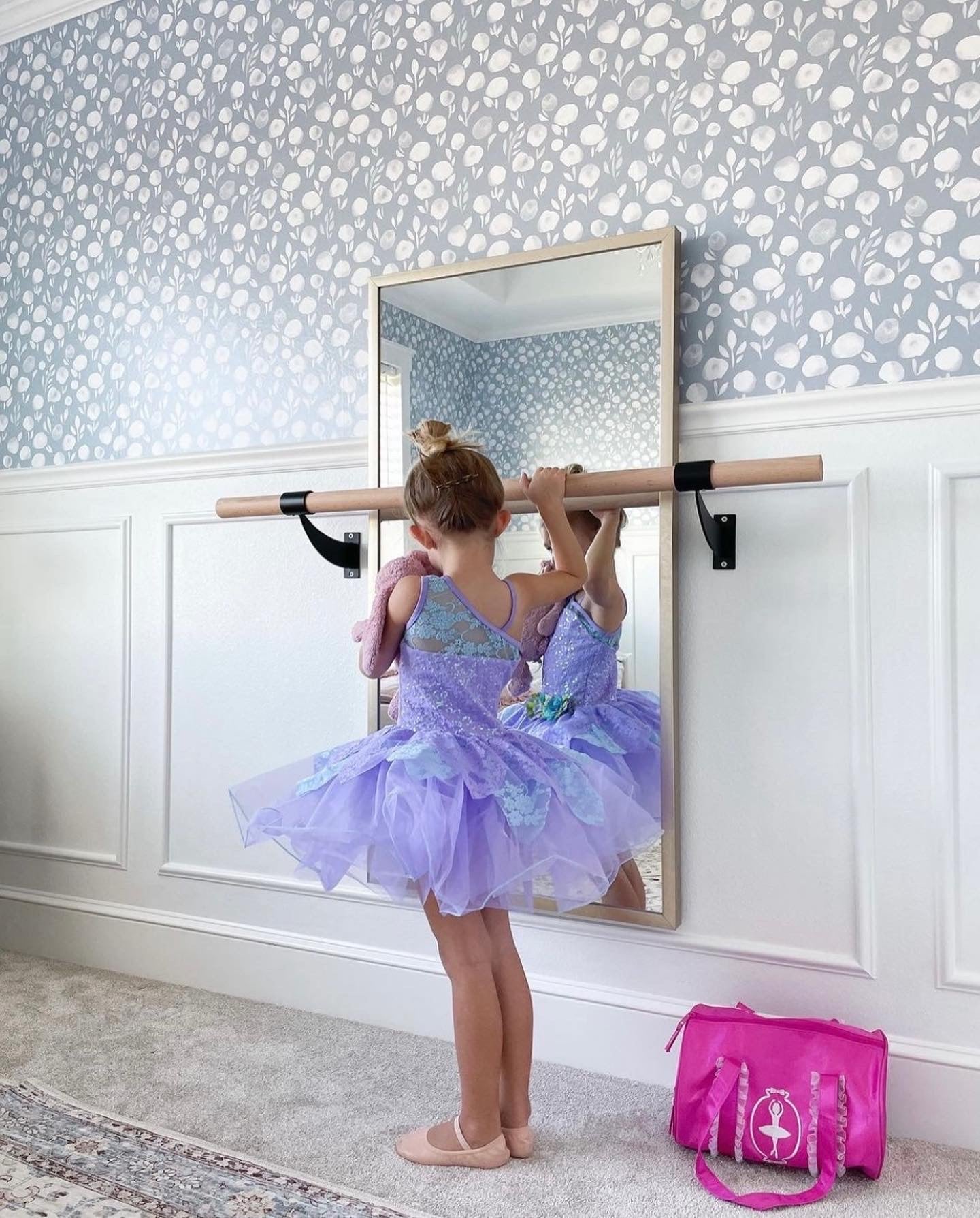 A young ballerina practices her pose in front of a large mirror, with 'Subtle Botanica II - Inverted' wallpaper adorning the wall behind her, providing a delicate and inspiring backdrop that complements her graceful movements.