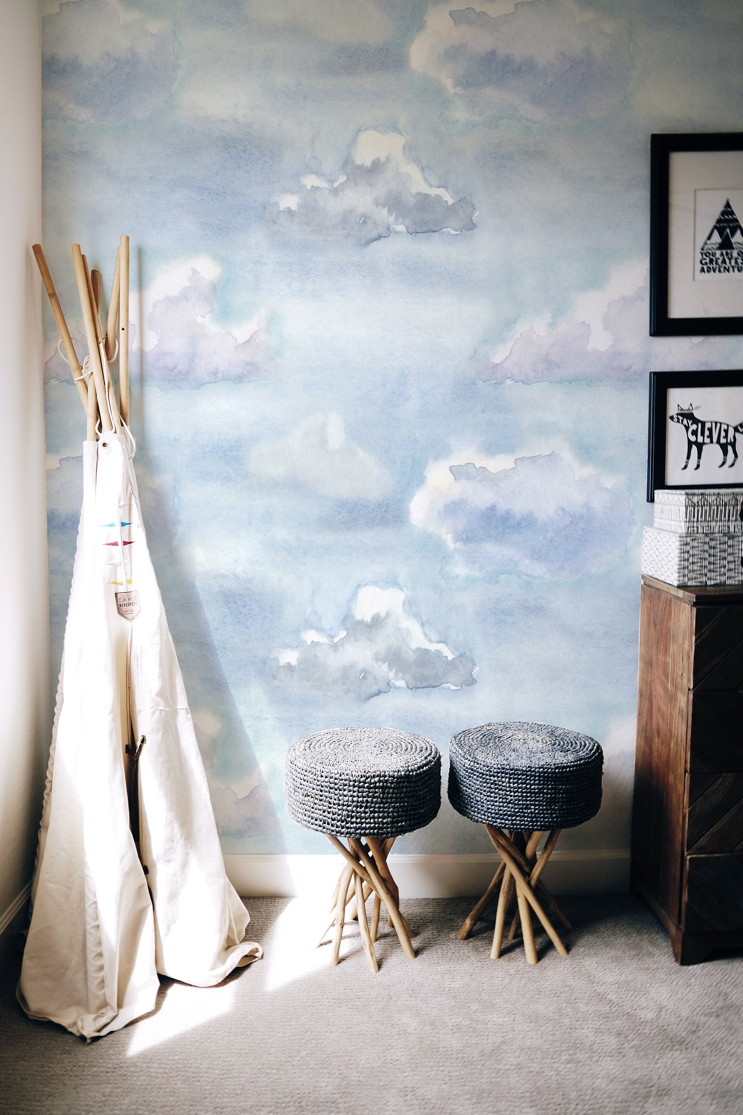  children's corner is transformed into a dreamy space with the "Watercolour Cloud and Skies" wallpaper. A teepee tent, woven stools, and playful decor create an imaginative play area, inspired by the tranquil, cloud-filled sky design of the wallpaper.