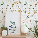 Interior design scene with a wall decorated with a floral and geometric pattern wallpaper, with botanical elements and golden shapes. In front, a wooden shelf holds a framed blank poster, a succulent in a wooden pot, and a spherical textured lamp