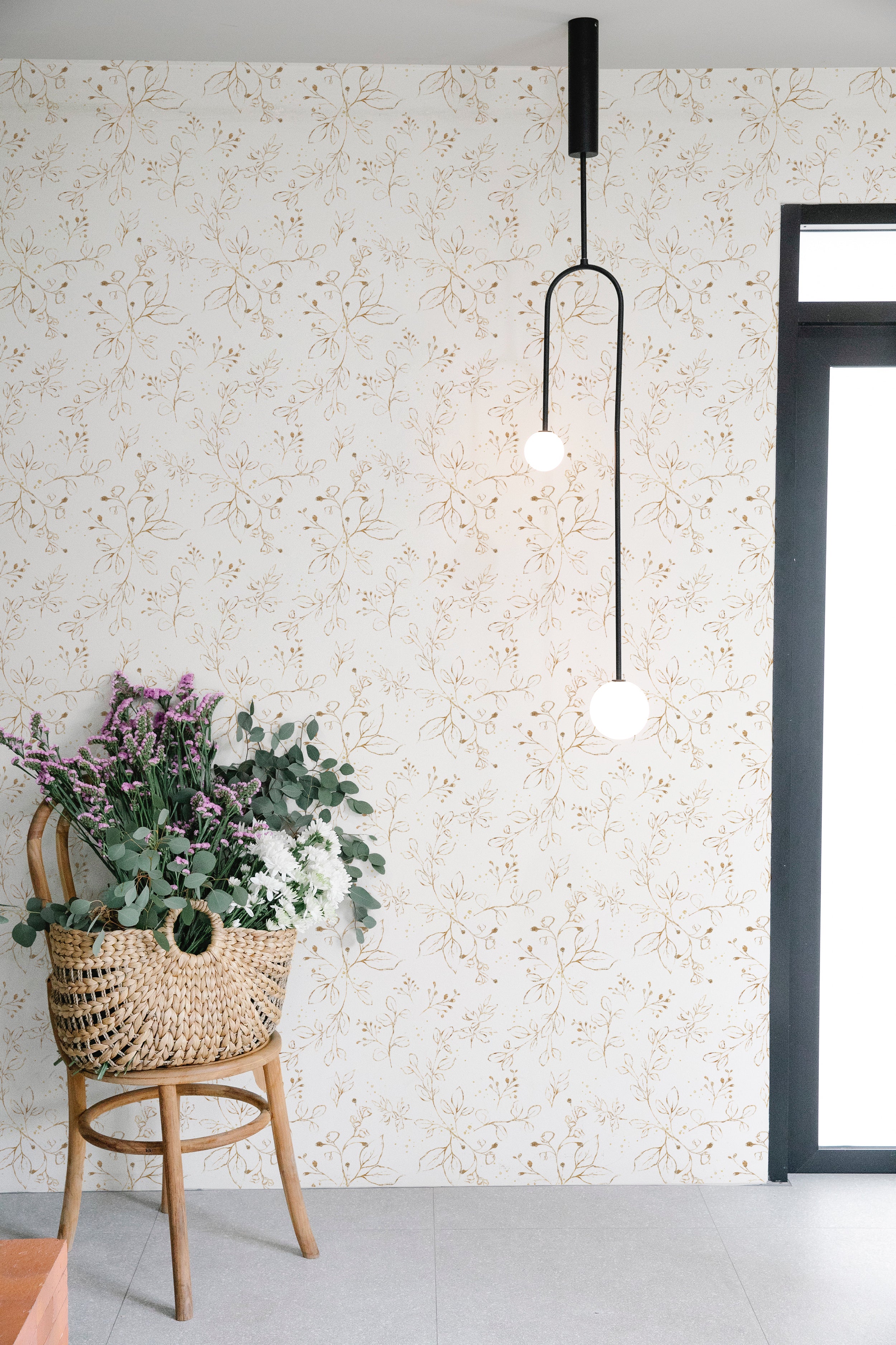 Modern interior design utilizing Gold Leaves Wallpaper, where the golden botanical illustrations provide a refined backdrop to a contemporary room with pendant lighting and a basket of fresh flowers.