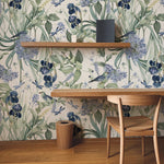 An elegant workspace featuring the 'Mint Floral Wallpaper - 50"', which showcases lush botanical prints with deep blue flowers and light green foliage, complemented by a wooden desk, chair, and shelving that enhances the natural theme.
