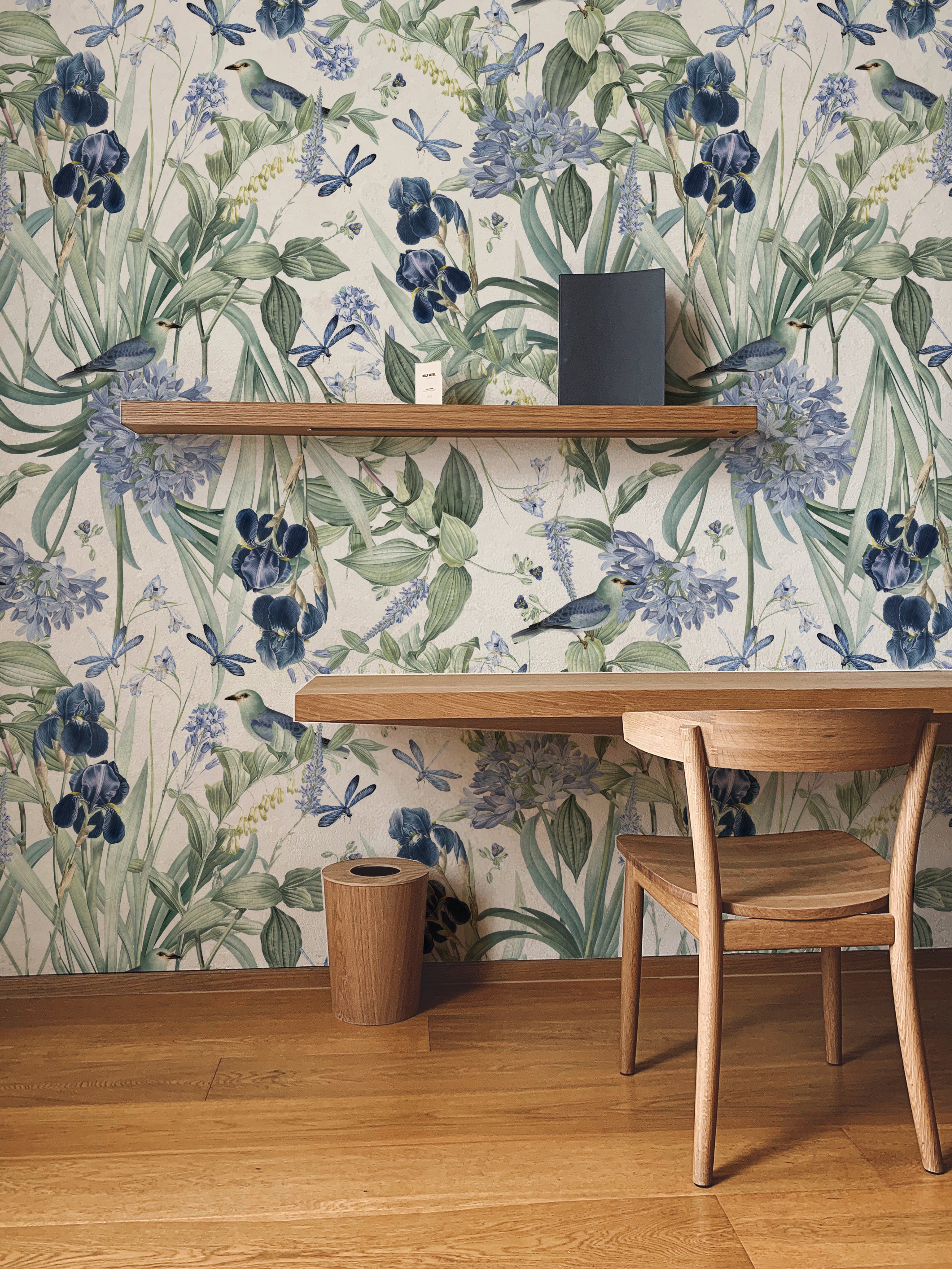 An elegant workspace featuring the 'Mint Floral Wallpaper - 50"', which showcases lush botanical prints with deep blue flowers and light green foliage, complemented by a wooden desk, chair, and shelving that enhances the natural theme.