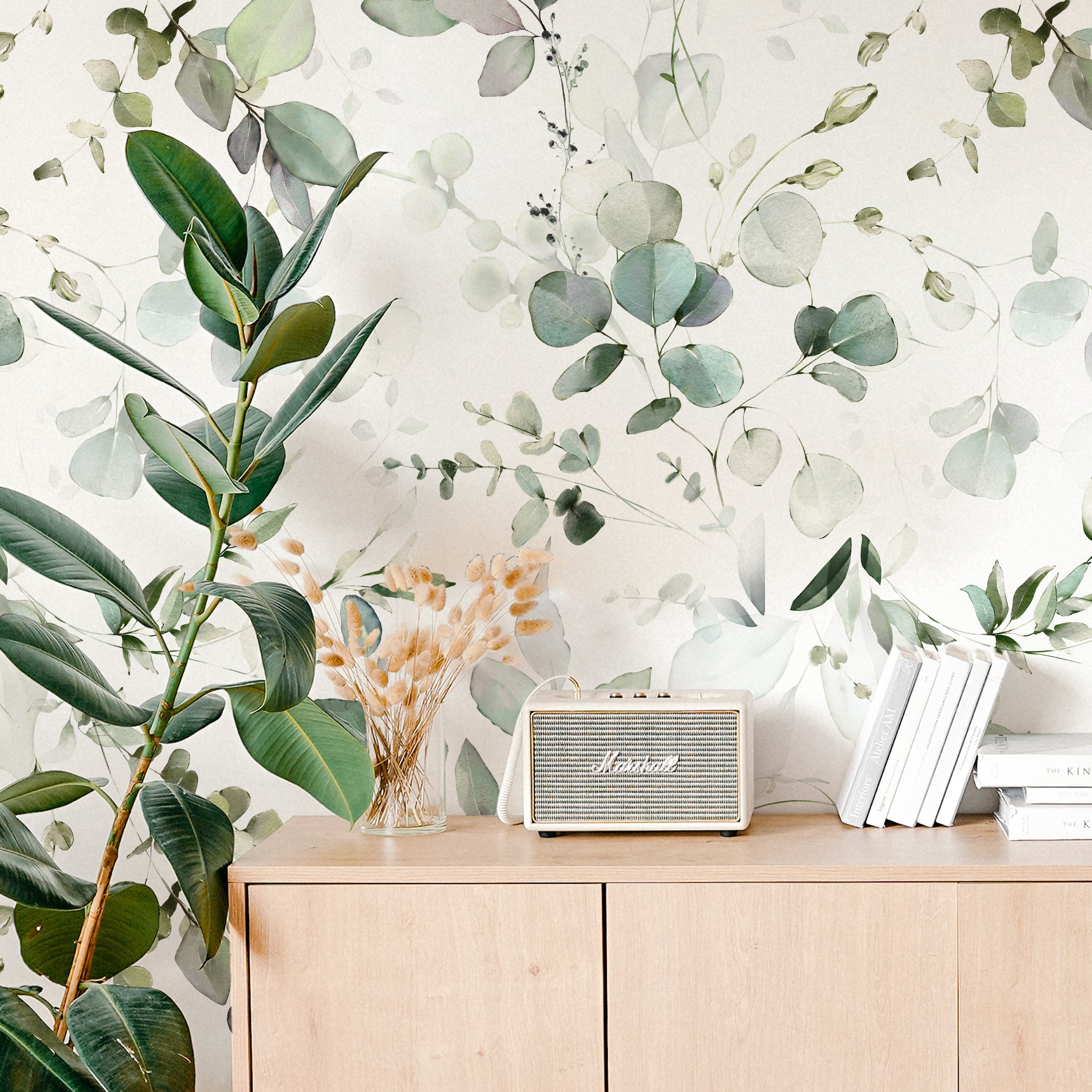A cozy corner featuring the Eucalyptus Wallpaper as a backdrop to a wooden sideboard adorned with a vintage radio, decorative wheat stalks in a vase, books, and a flourishing potted plant that complements the wallpaper's botanical theme.