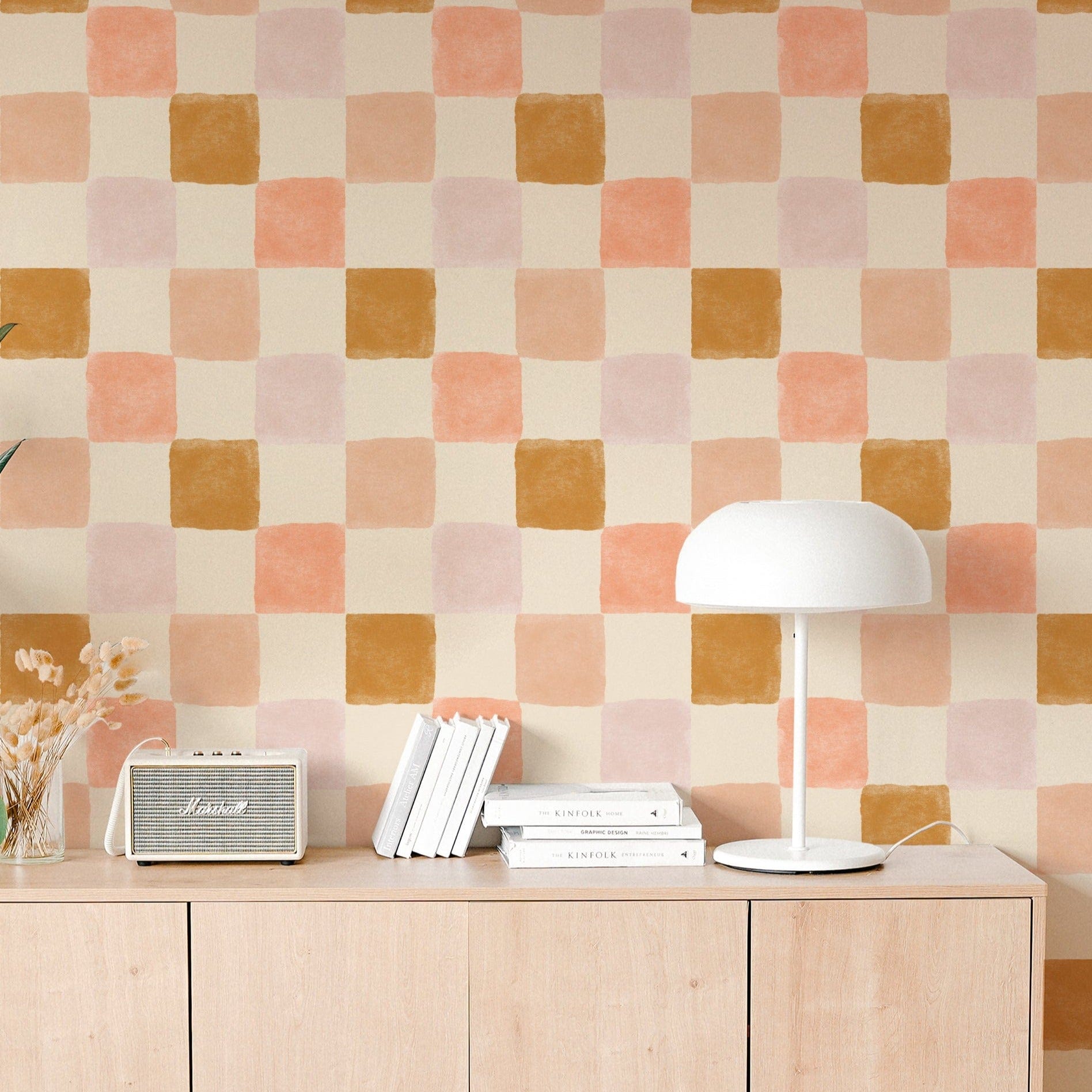 Charlotte Wallpaper in a contemporary living space, featuring large checkered patterns in shades of peach, gold, and light pink on a cream background, enhancing the room's modern aesthetic with natural wood furniture and minimalist decor