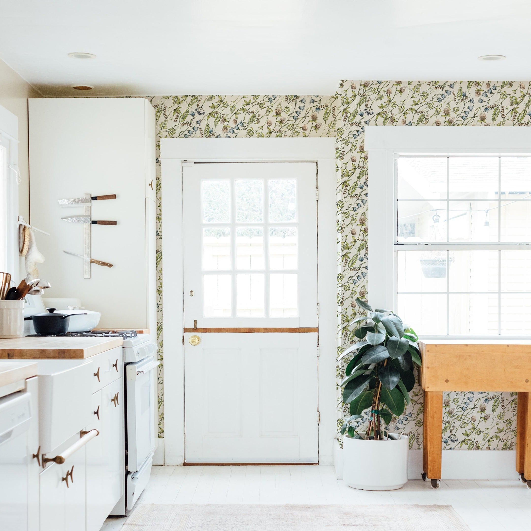 A cozy kitchen interior with a rustic charm, where the 'Watercolour Botanical Wildflowers' wallpaper adds a vibrant touch to the walls. The pattern is full of delicate floral illustrations that bring an organic and serene feel to the space. Natural light streams through a window, enhancing the room's homey atmosphere.