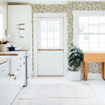 A cozy kitchen interior with a rustic charm, where the 'Watercolour Botanical Wildflowers' wallpaper adds a vibrant touch to the walls. The pattern is full of delicate floral illustrations that bring an organic and serene feel to the space. Natural light streams through a window, enhancing the room's homey atmosphere.
