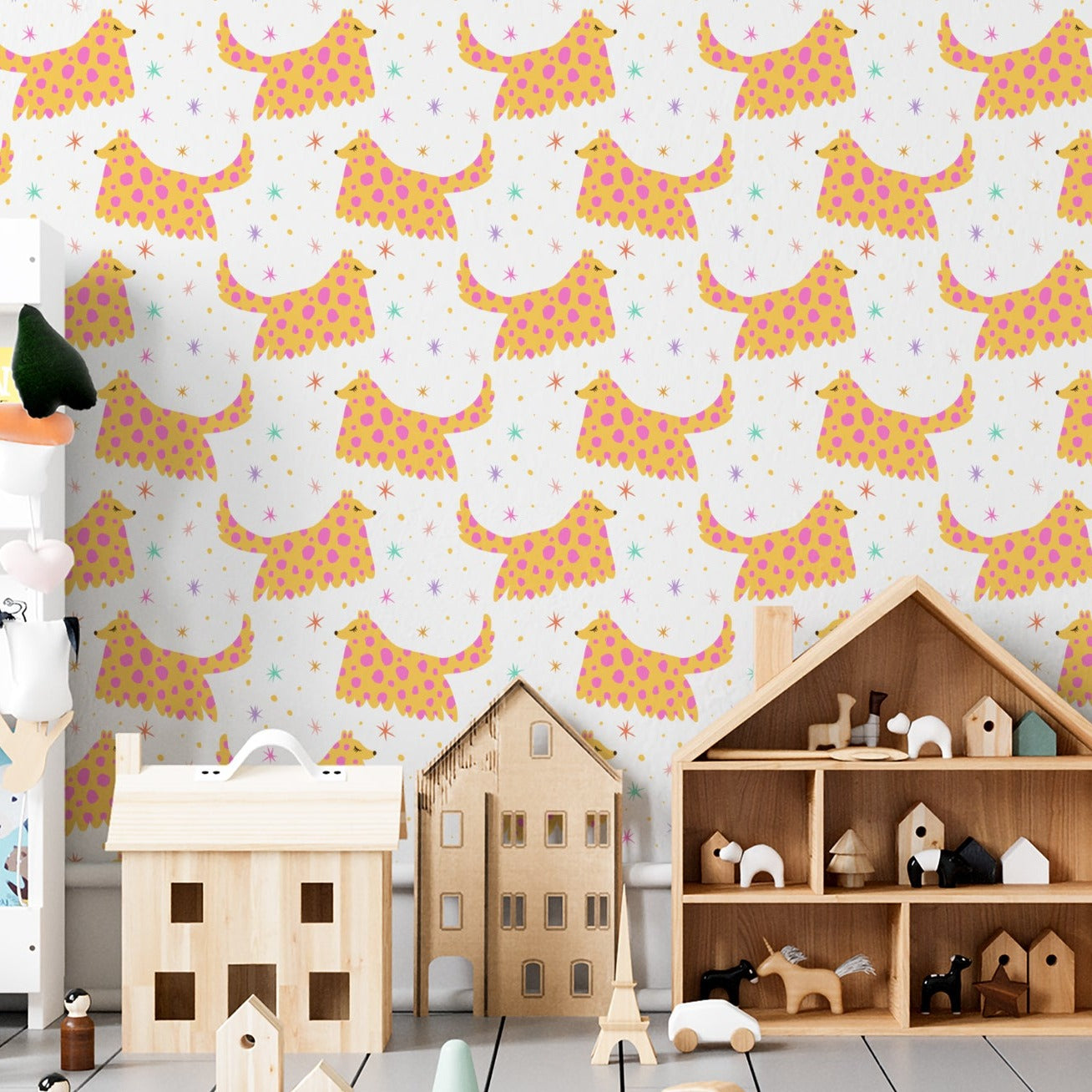 A children's playroom decorated with 'Dog Wallpaper 35,' showcasing walls covered in a repeating pattern of whimsical, spotted dogs in pink and yellow on a white background, complemented by a variety of children's toys and books