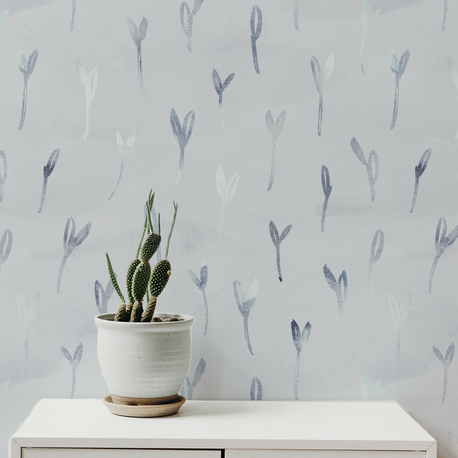 Floral Foil Wallpaper displayed in a room setting, enhancing the room's decor with its light, ethereal plant motifs in soothing colors, complemented by minimalist furniture and a potted cactus.