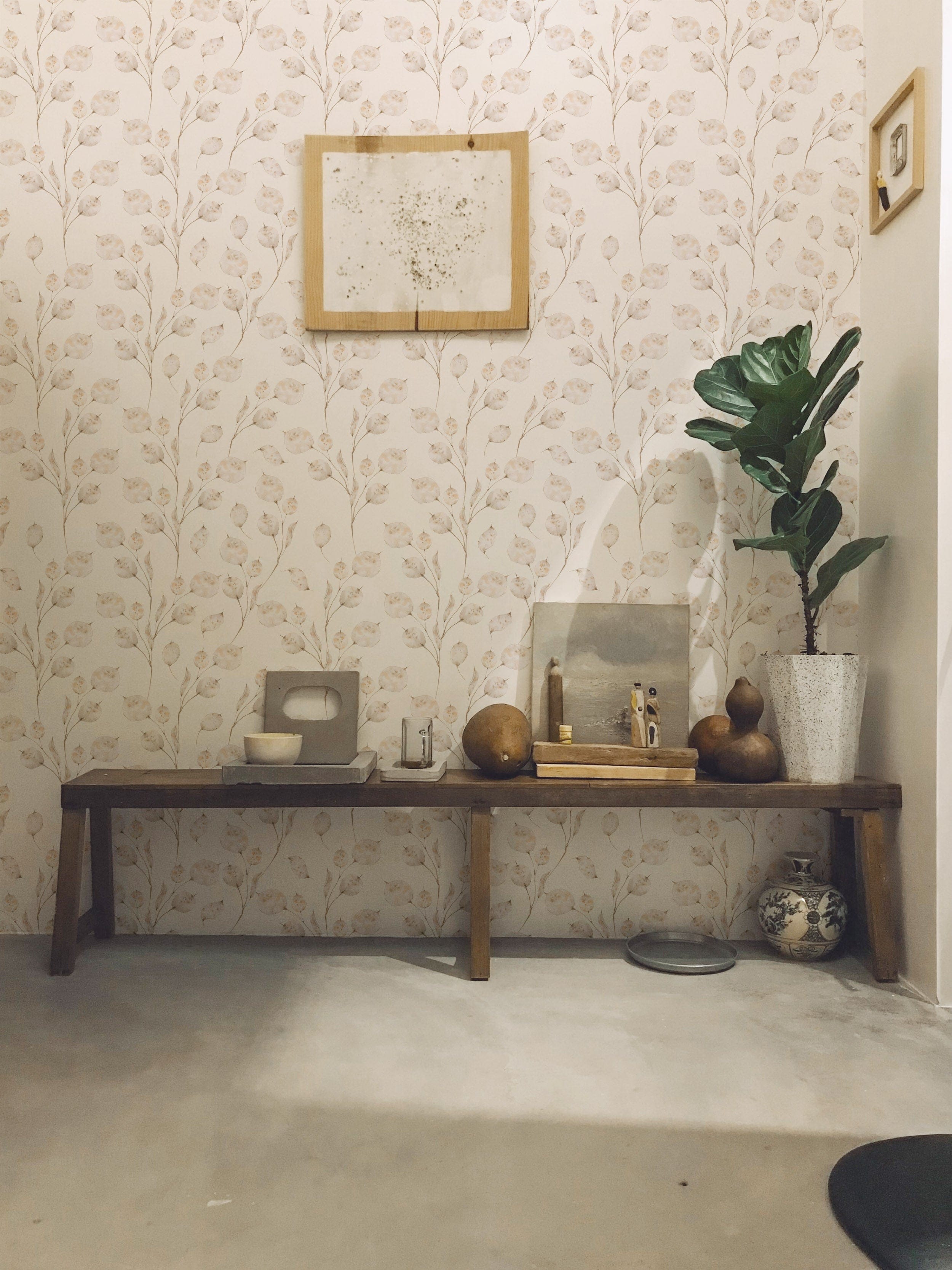 A cozy entryway featuring Winter Branches Wallpaper with delicate, beige botanical designs on a white background, accompanied by a wooden bench, a potted plant, and various decorative items.