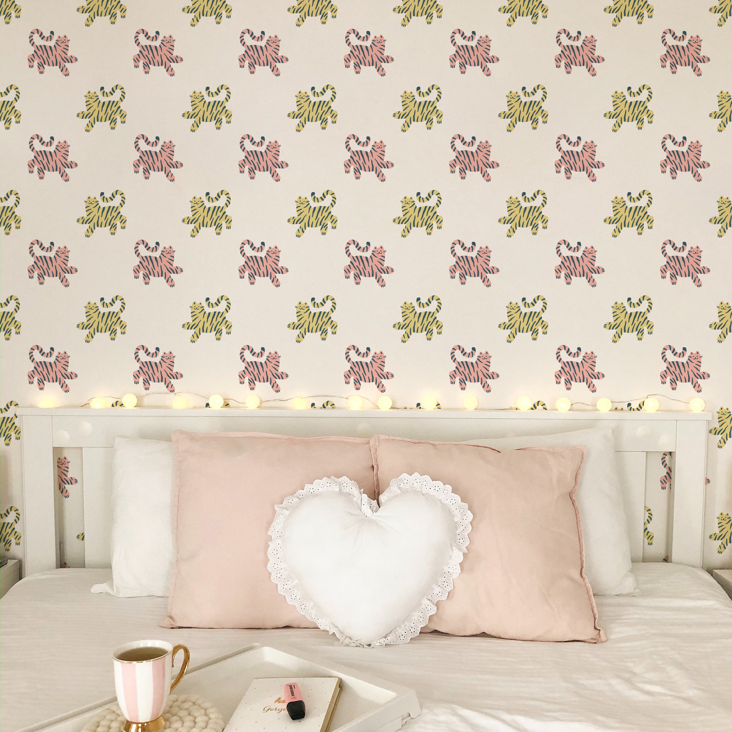Charming children's room setup showcasing 'Cat Wallpaper 3' with leaping pink and yellow cats on the walls. The room is adorned with a heart-shaped white pillow and soft pink cushions, creating a warm and welcoming atmosphere