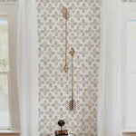 An inviting corner of a room displays the "Moroccan Tile - Beige" wallpaper, which serves as a warm and stylish backdrop for a round side table and a decorative golden arrow wall piece. The gentle beige hues of the wallpaper pattern provide a neutral yet decorative background, illustrating how it can seamlessly integrate into a home's decor.