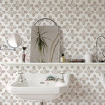 This bathroom interior features the "Moroccan Tile - Beige" wallpaper, with a classic beige and white Moroccan tile pattern that adds an air of sophistication and worldly charm. The wallpaper complements the white pedestal sink and the reflective surface of a rectangular mirror, alongside various bathroom accessories, creating a harmonious and elegant space.