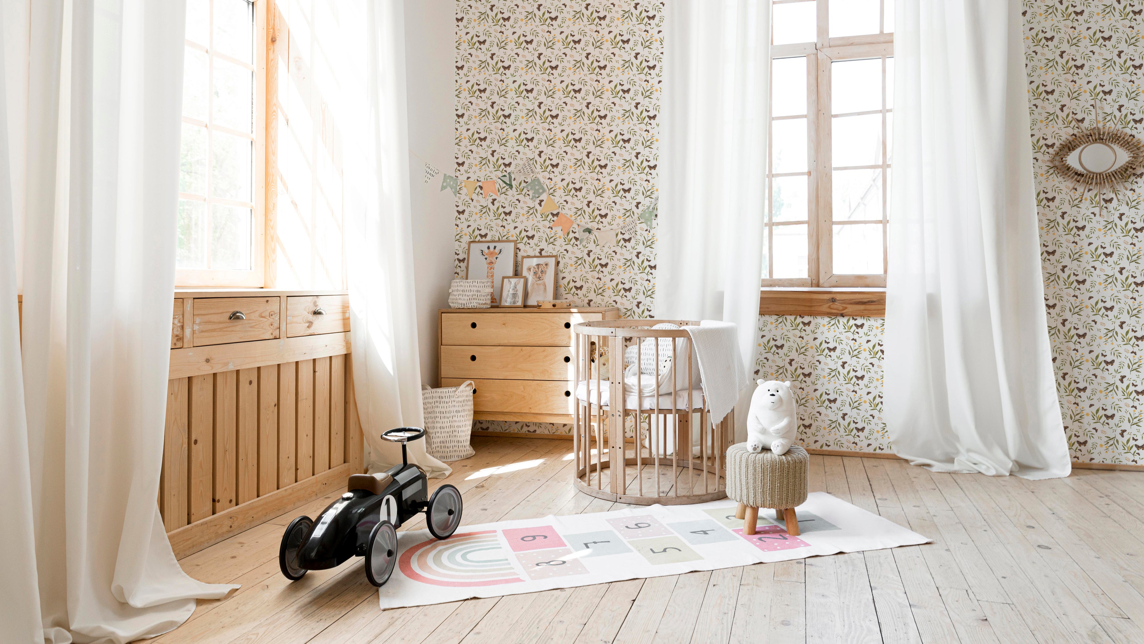 A children's nursery room beautifully adorned with Butterfly Floral Wallpaper. The wallpaper's pattern of brown butterflies, yellow flowers, and green leaves adds a playful and refreshing touch to the space, complemented by wooden furniture and a large window.