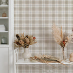 A bright and airy corner of a room featuring Winter Plaid Wallpaper with a large bookshelf and a side table decorated with dried flowers. The wallpaper's subtle plaid pattern in beige and white offers a cozy backdrop that complements the natural textures and soft color palette of the decor.