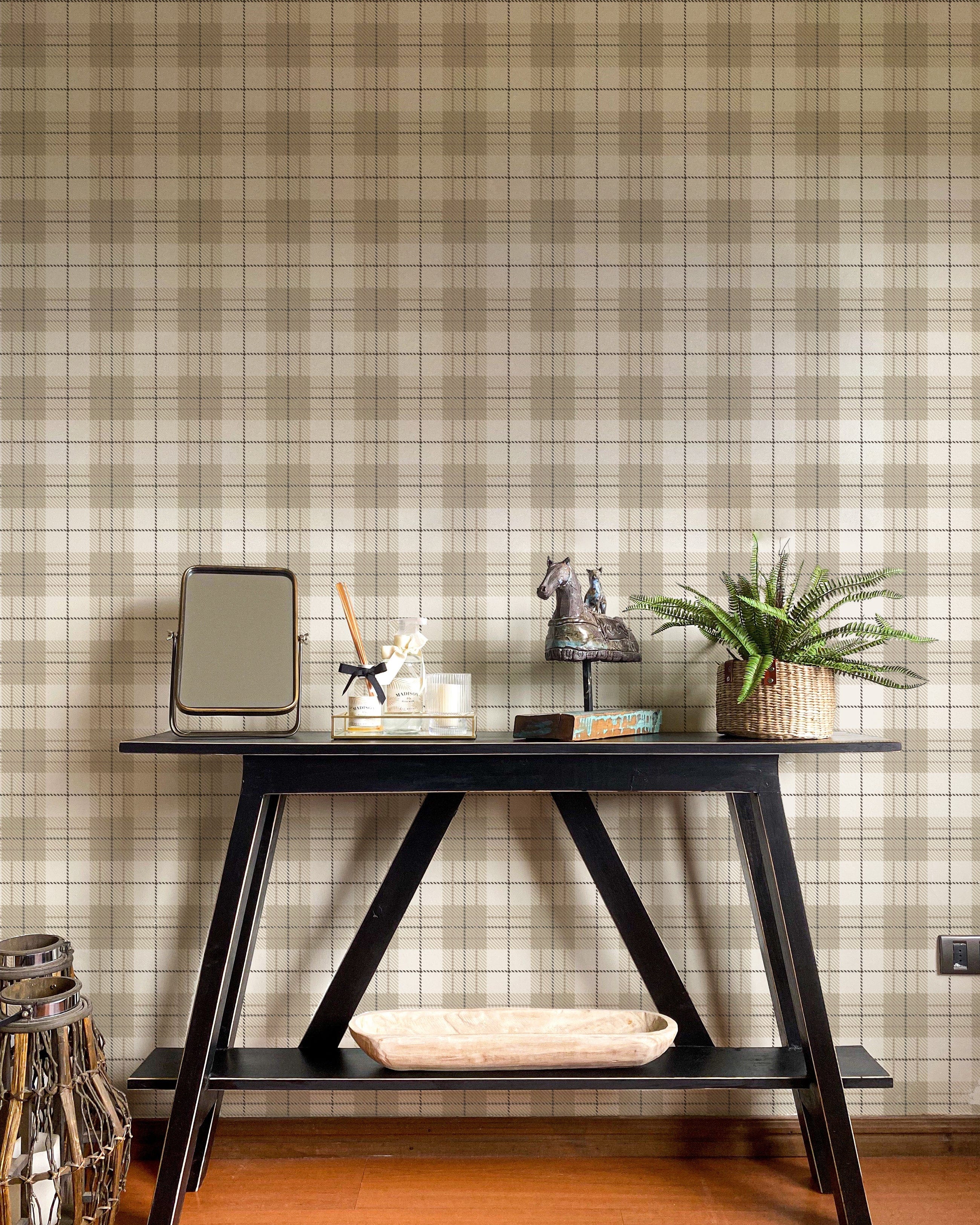 A chic home office area showcasing Winter Plaid Wallpaper as the backdrop, with a dark, angular wooden desk adorned with home decor items, contrasting the wallpaper's timeless plaid design in soft, warm tones, creating a sophisticated and inviting workspace.