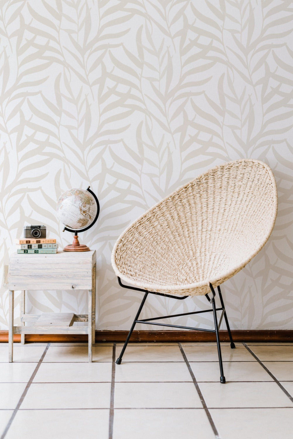 Interior design setting with 'Earthy Wallpaper' covering the wall, complemented by a rustic white sidetable with a globe and camera on top, and a woven rattan chair in the foreground, all contributing to a peaceful, earthy vibe.