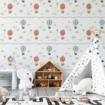 A playful nursery room featuring Balloon Adventure Wallpaper, adorned with whimsical illustrations of hot air balloons, kites, and clouds in pastel colors. The room is decorated with child-friendly furniture and toys, creating an imaginative space for little ones.