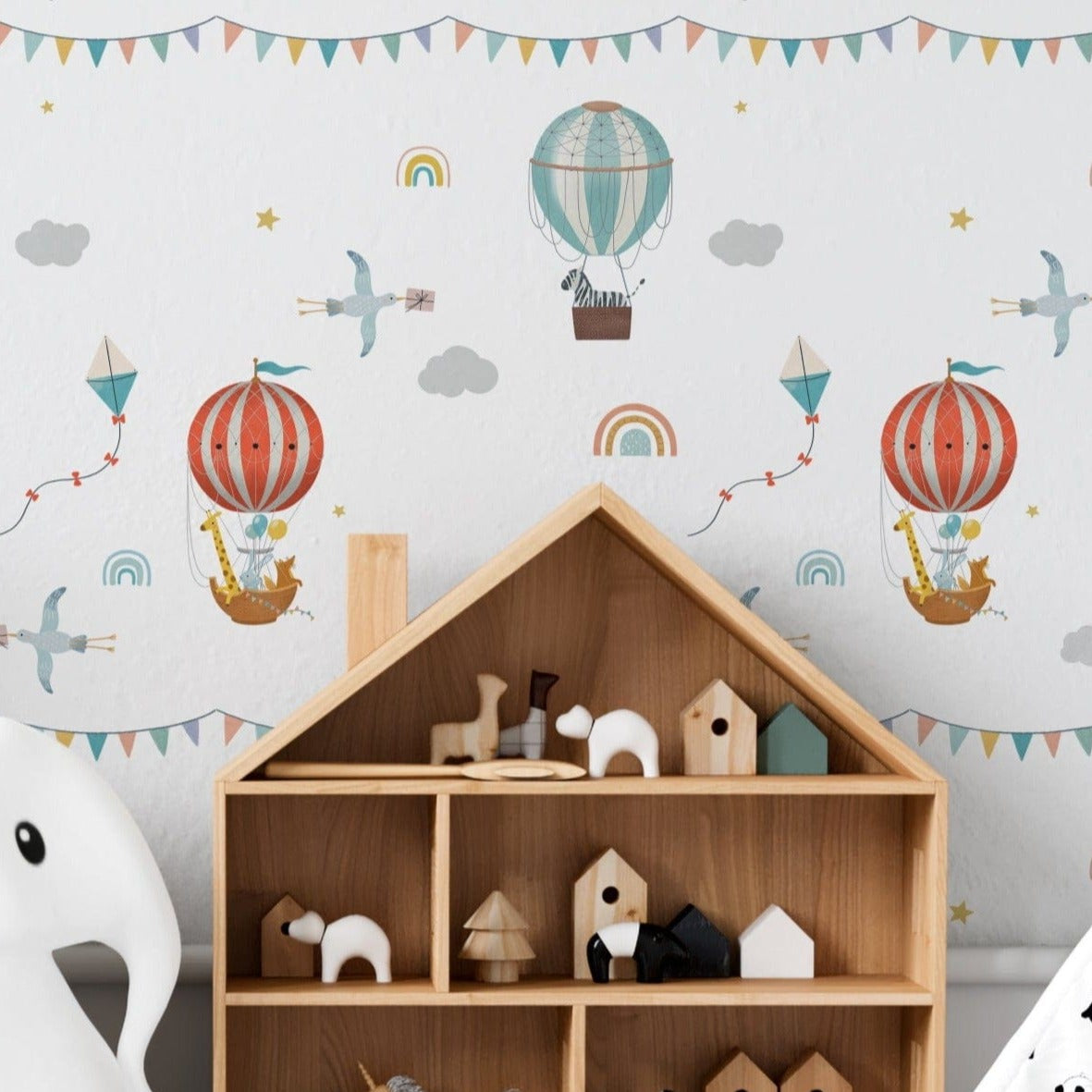 A playful nursery room featuring Balloon Adventure Wallpaper, adorned with whimsical illustrations of hot air balloons, kites, and clouds in pastel colors. The room is decorated with child-friendly furniture and toys, creating an imaginative space for little ones.