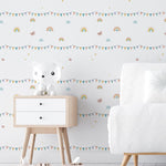 A nursery room wall decorated with the Rainbow Adventure wallpaper showcasing pastel rainbows, bunting flags, and twinkling stars, providing a joyful and stimulating environment for a child