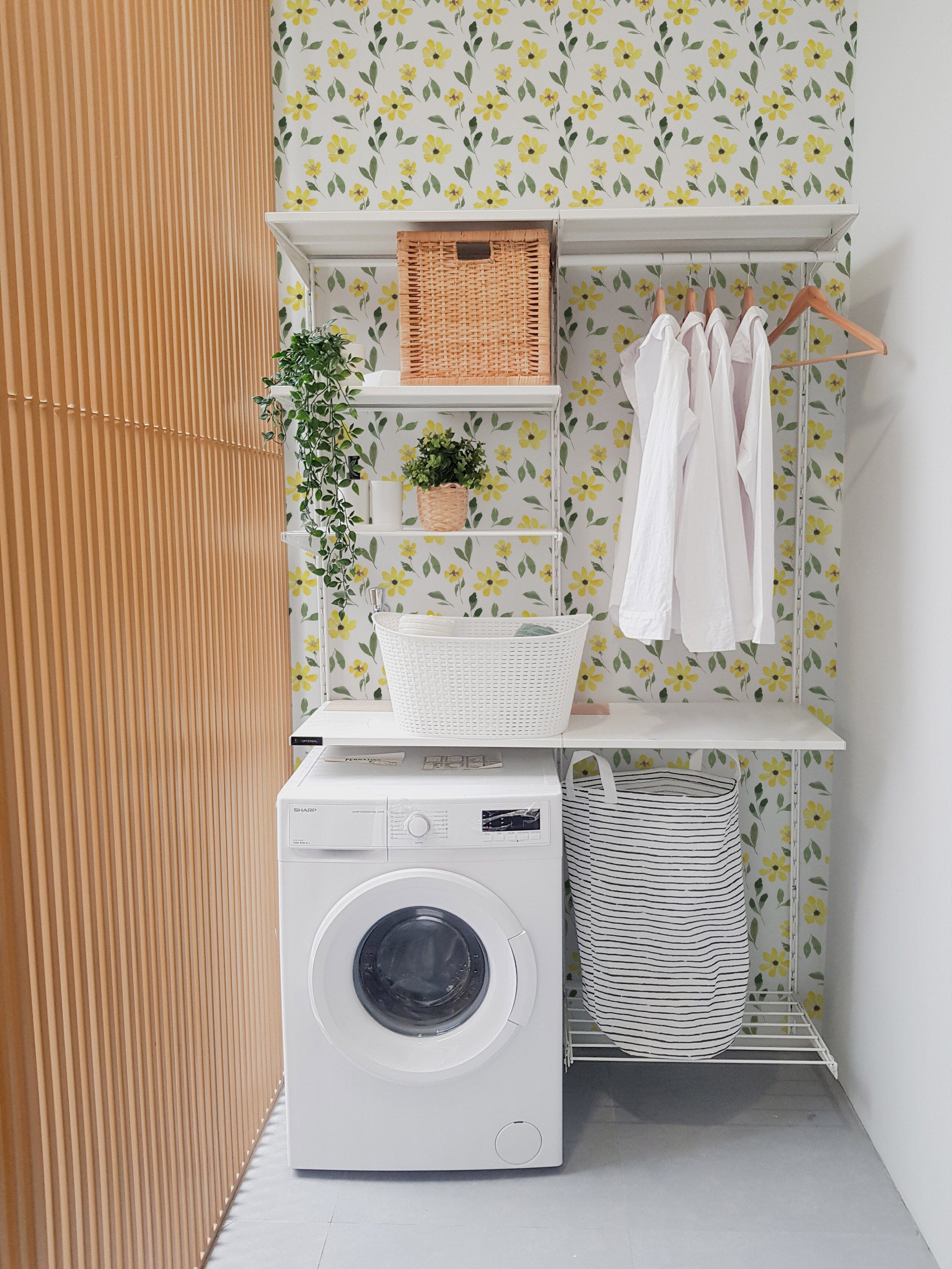 Modern laundry room with a washing machine, wooden shelving, and baskets, featuring Yellow Spring Wallpaper with watercolor yellow flowers and green leaves
