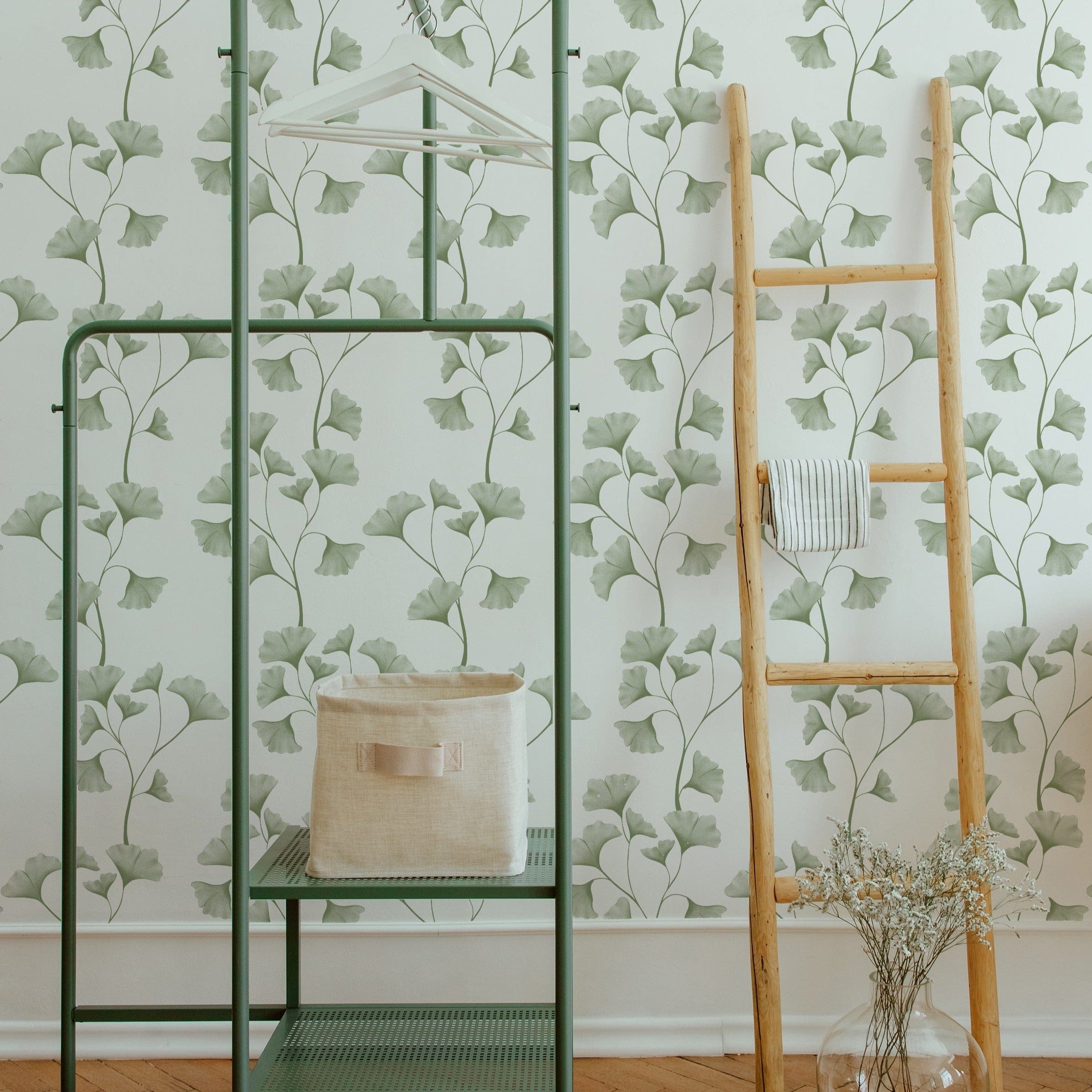 A styled interior scene where the Botanical Vines Wallpaper is used to decorate a bright, airy room. The wallpaper covers the walls behind a modern green metal shelving unit and a wooden ladder, both adorned with neutral-toned decor items, contributing to a refreshing and organic atmosphere.