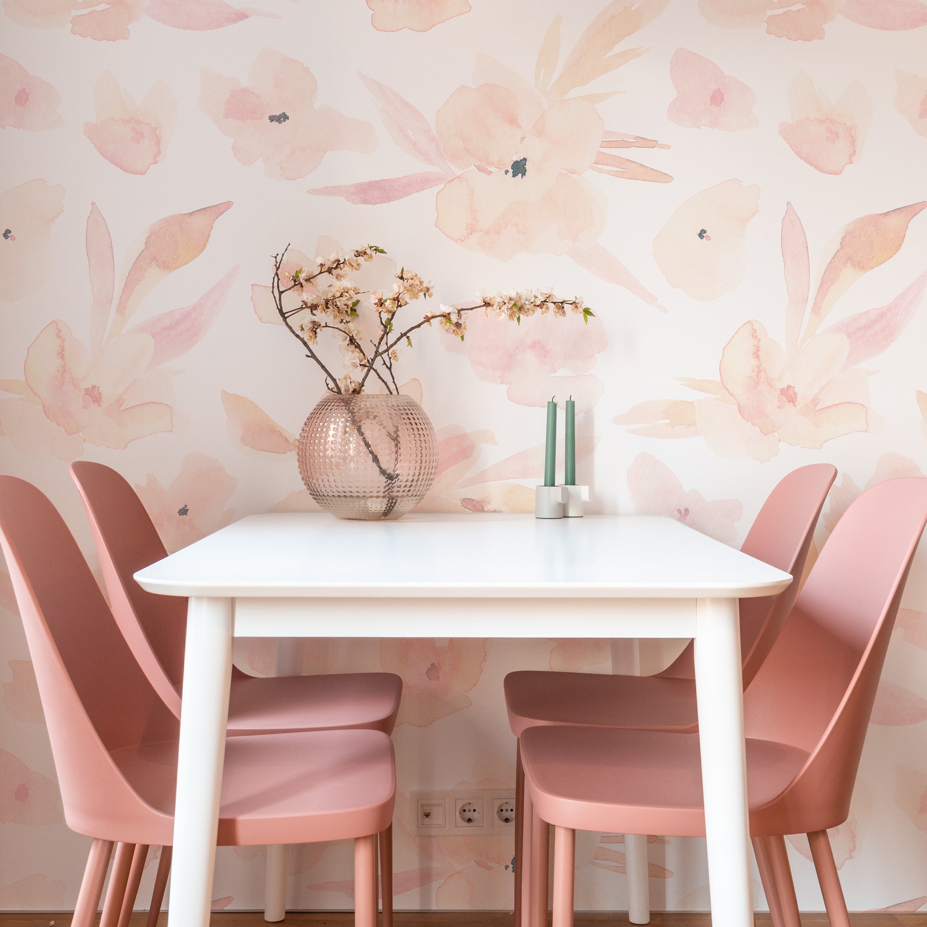 A bright and airy dining area featuring a white table and soft pink chairs, complemented by the subtle elegance of the Florelegance Wallpaper, which boasts large watercolor flowers in shades of pale pink and cream, creating a serene backdrop