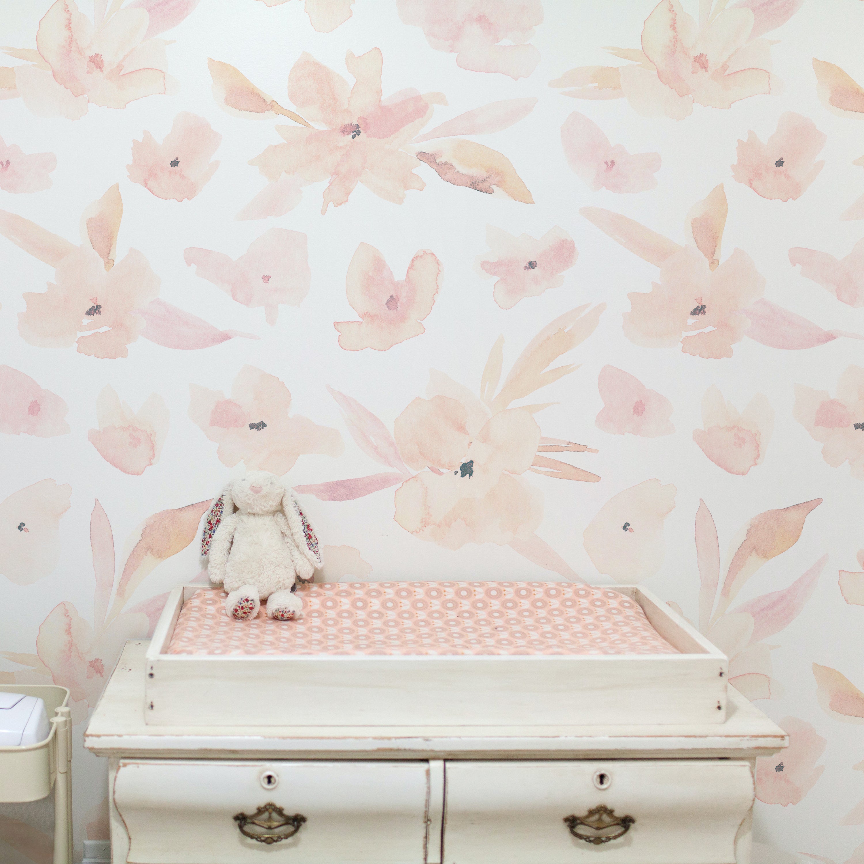 A charming nursery corner with the Florelegance Wallpaper adorning the walls, accompanied by a vintage white changing table and a cuddly stuffed rabbit, enhancing the room's soothing and graceful aesthetic.