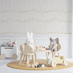 A child's playroom with Boardwalk Wallpaper on the walls, displaying vertical, uneven beige stripes on a light background. The room is furnished with a small wooden table and chairs, and toys, creating a playful and inviting space.