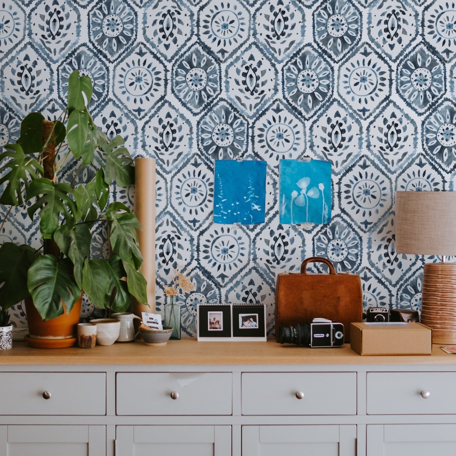 Home office space with a white cabinet adorned with personal items and green plants, set against a backdrop of Moroccan Tile wallpaper in shades of indigo blue.